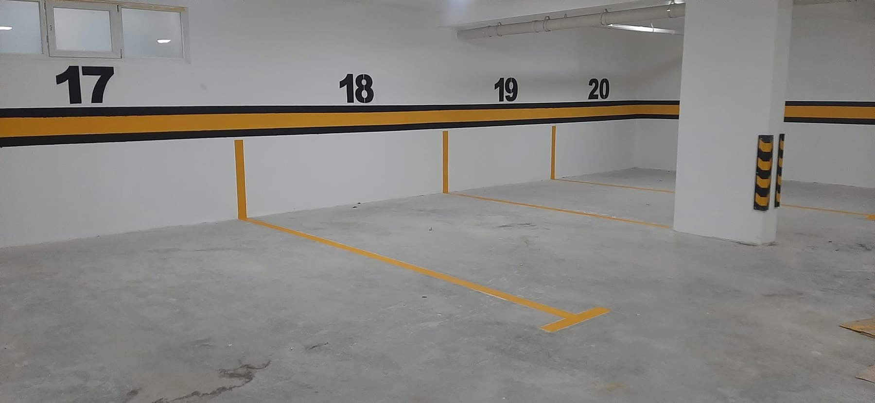 Vende parkimi të numëruara dhe të vijëzuara në një garazh të brendshëm, me mbrojtëse cepash të verdha e të zeza