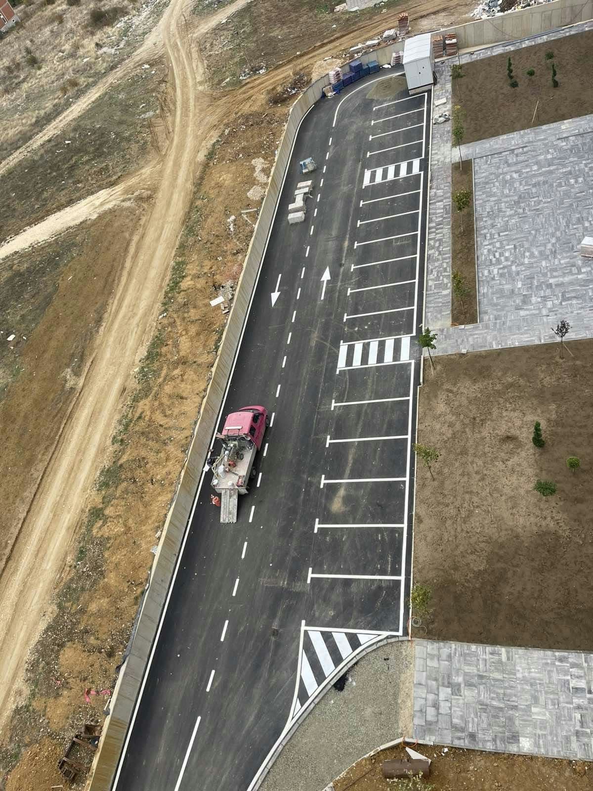 Pamje ajrore e sinjalistikës horizontale të sapo vendosur në një rrugë hyrëse, me vende parkimi dhe kalim këmbësorësh